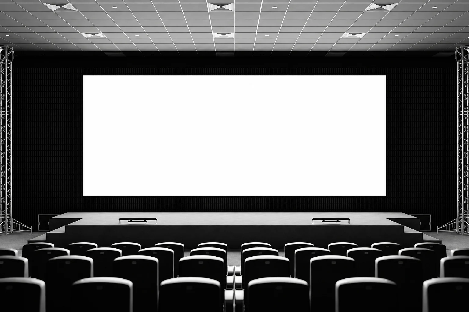 Blank white screen centered on a dark auditorium stage, framed by trusses and curtains with theater seats in front.