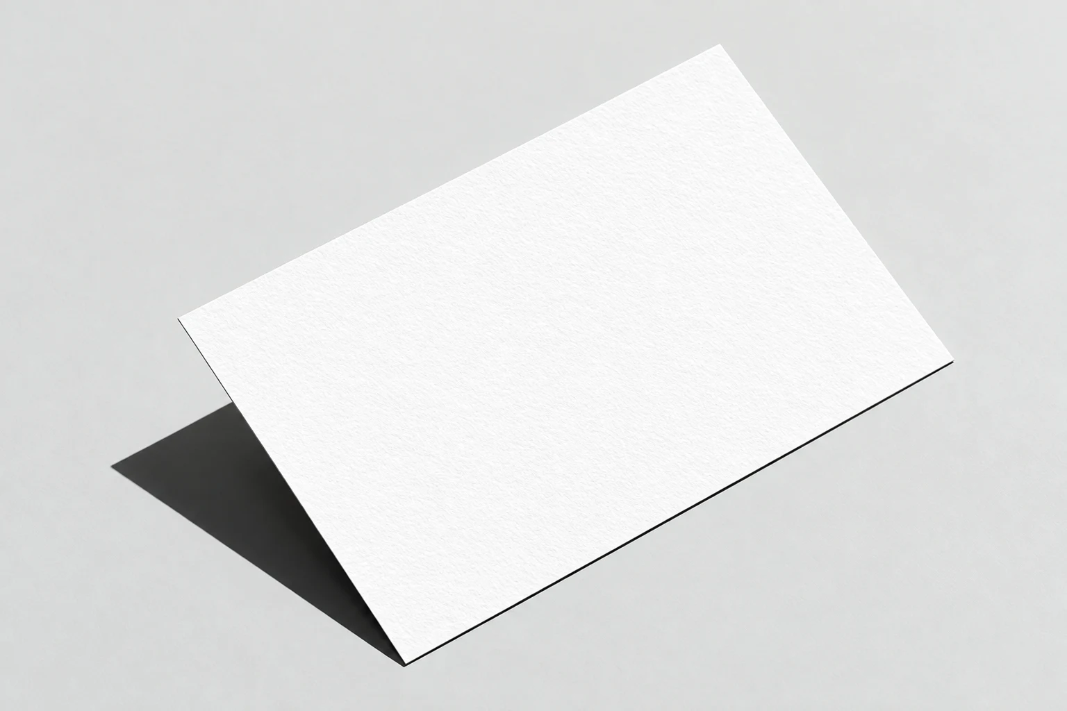 Angled, lightly textured white business card with subtle embossing and a dark shadow on a pale gray background.