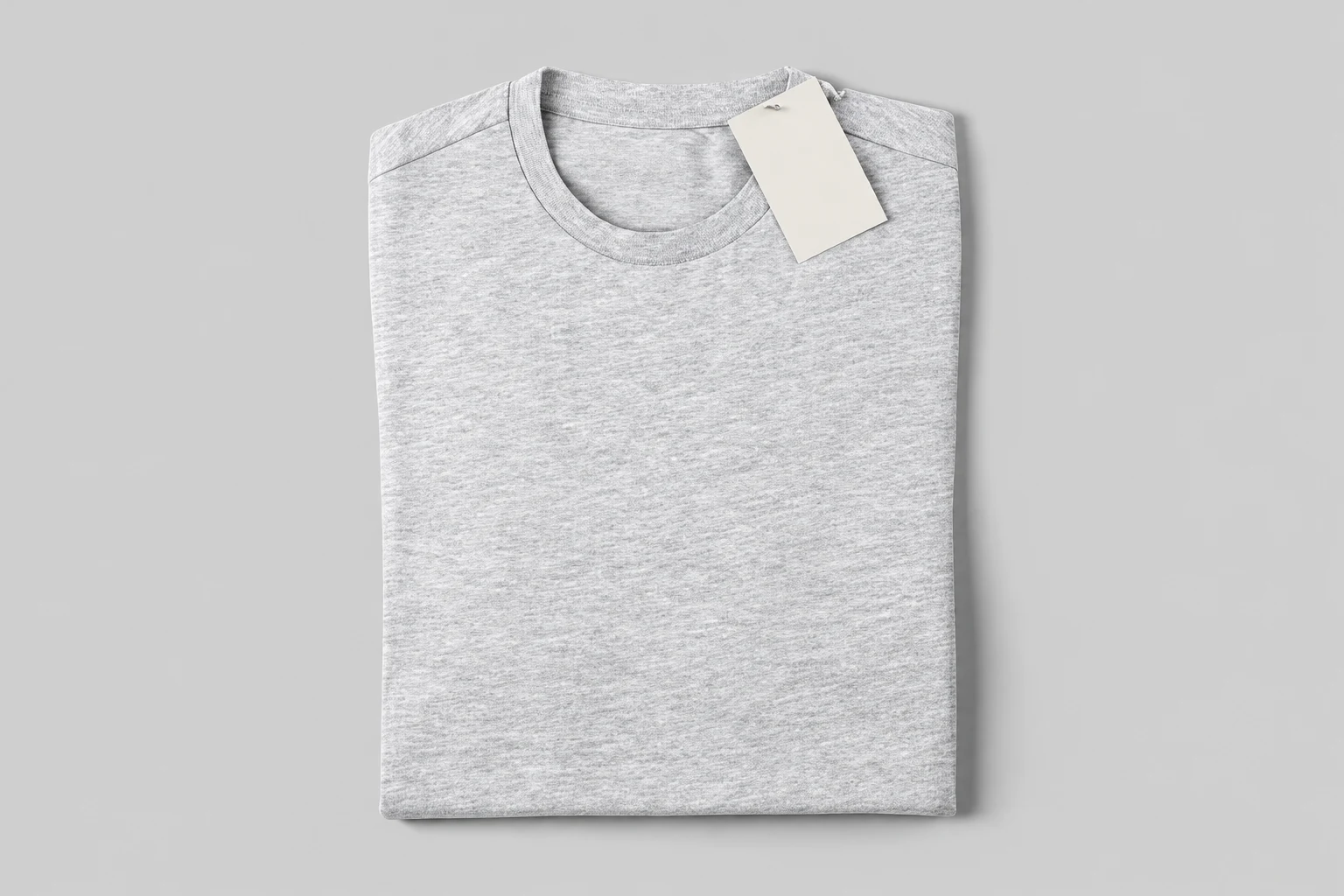 Top view of a folded light gray heather T-shirt with a blank white tag near the collar on a pale gray background.
