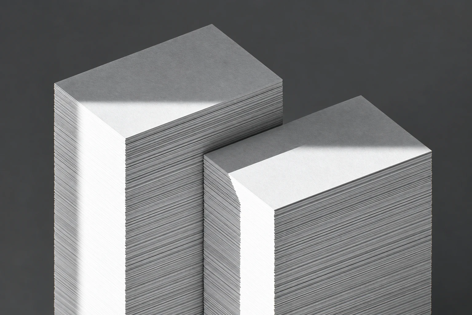 Two thick stacks of blank white business cards on a dark charcoal background, viewed from above at an oblique angle.