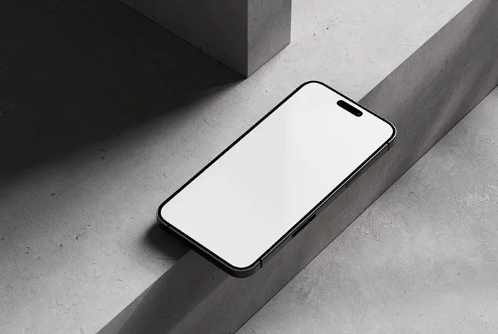 Blank-screen black-edged smartphone resting diagonally on a concrete ledge under directional light.