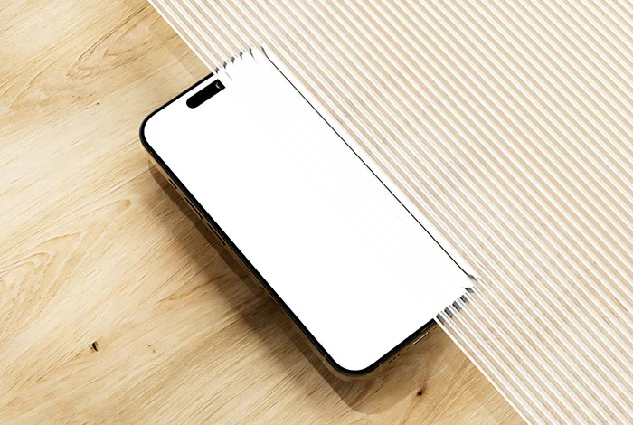 Black-edged smartphone with a blank white screen beneath ridged glass on a pale wood tabletop.
