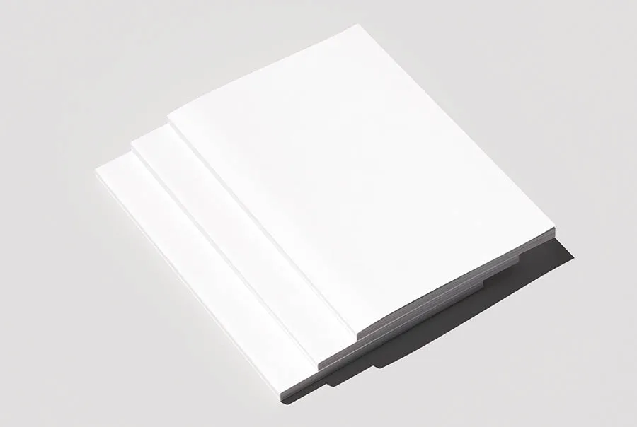 Stack of closed magazines with plain white covers, viewed from above at an angle on a pale gray background.